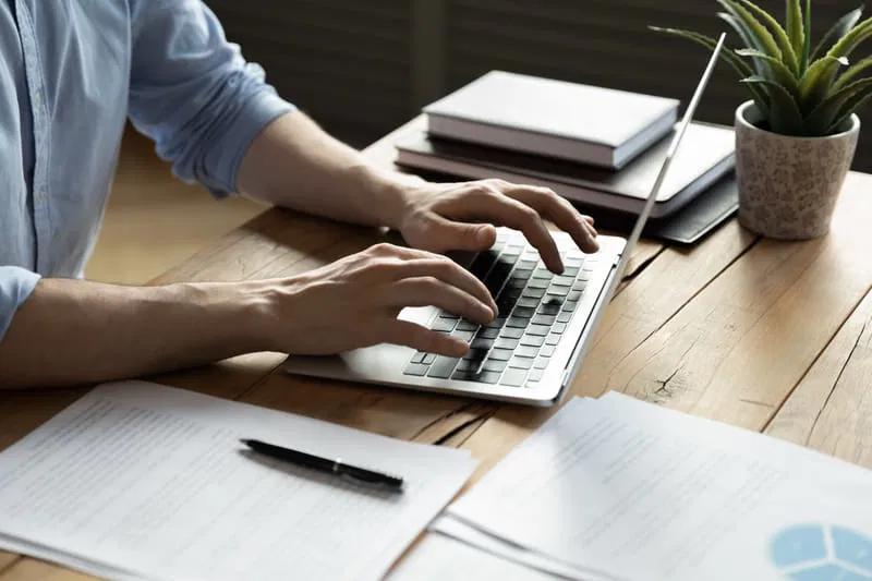 Personne travaillant sur un ordinateur portable dans un bureau en bois ordonné.