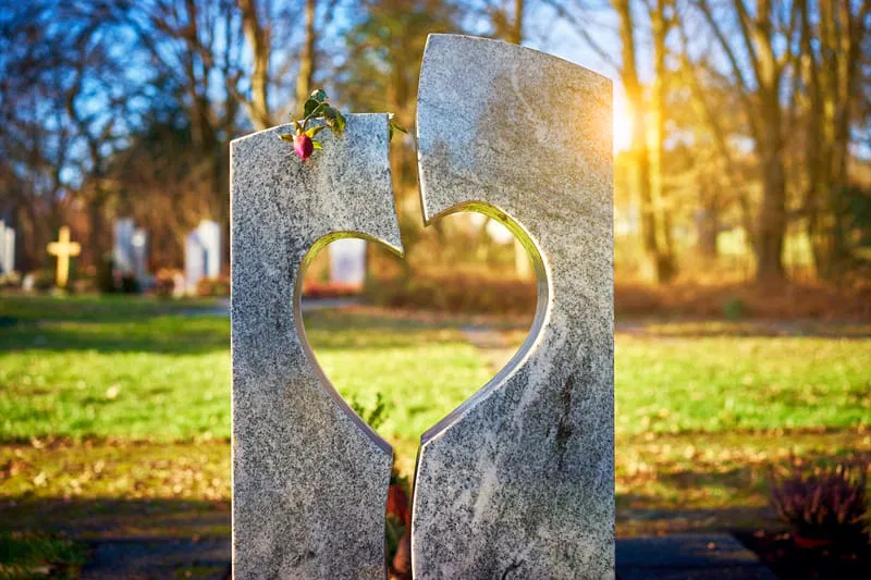 Pierre tombale en granit sculptée d'un cœur évidé sous un rayon de soleil.