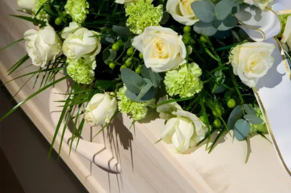 Arrangement floral de roses blanches et œillets verts sur un cercueil clair.