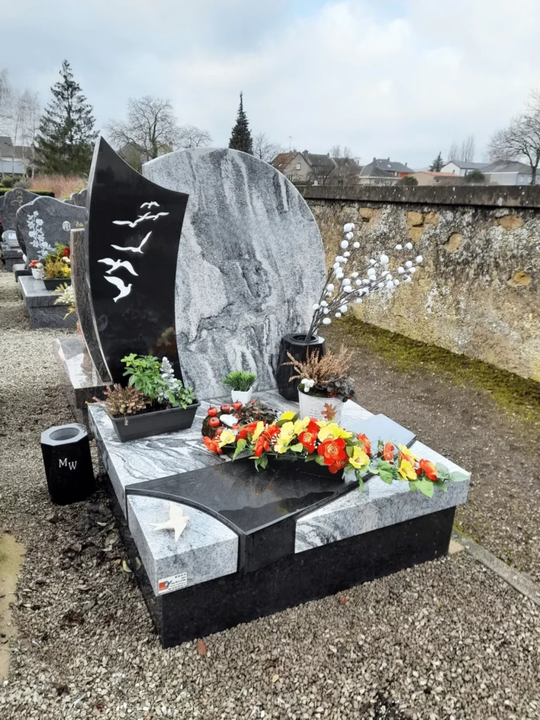 Monument cinéraire contemporain en granit veiné avec gravures d'oiseaux.