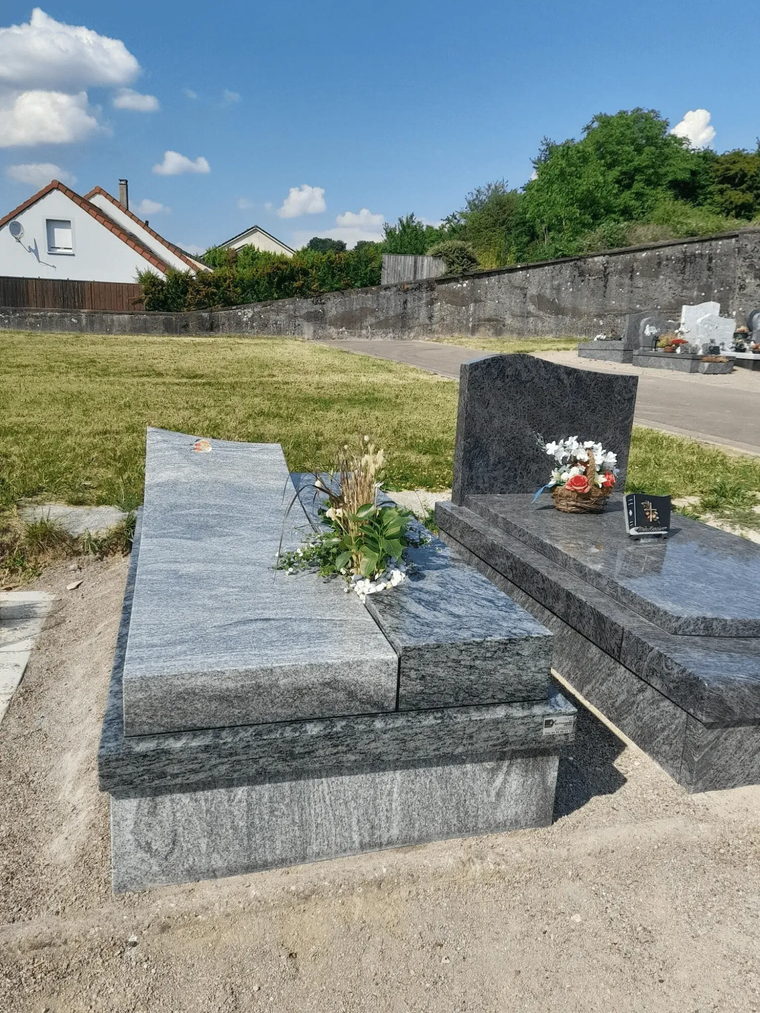 Monument funéraire contemporain en granit gris veiné avec composition florale.