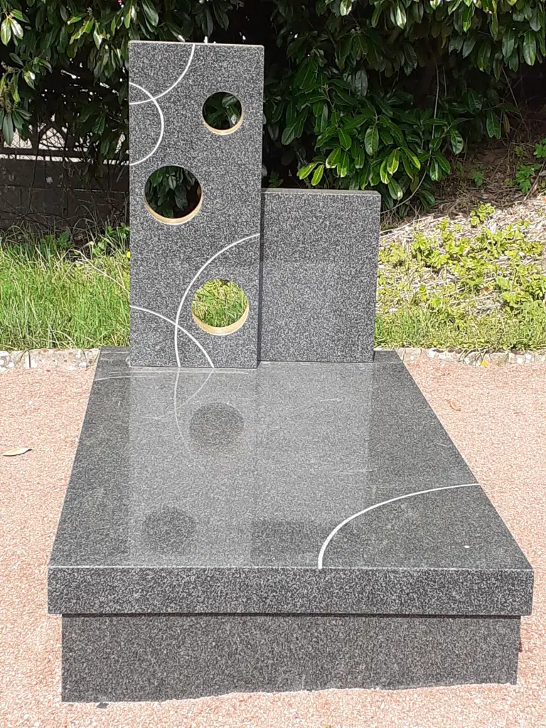 Monument funéraire moderne en granit gris orné de motifs circulaires.
