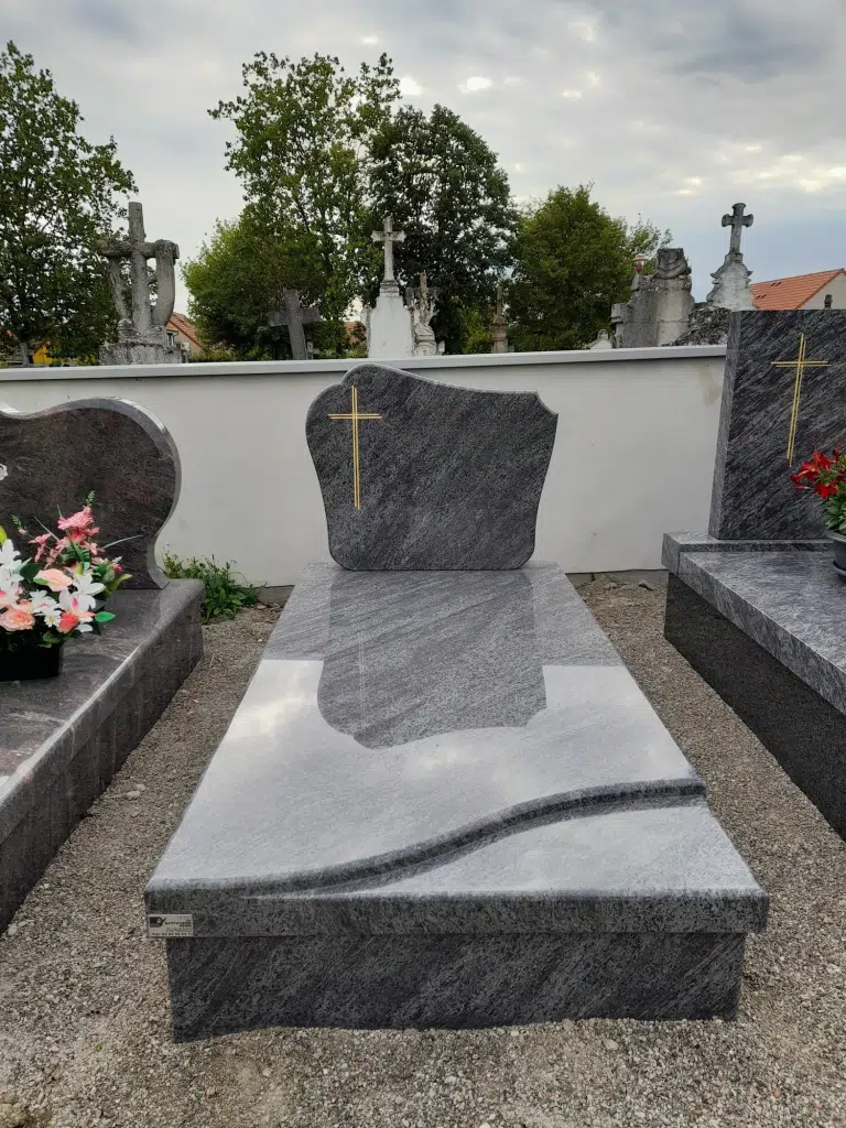 Pierre tombale en granit gris veiné surmontée d'une croix dorée.