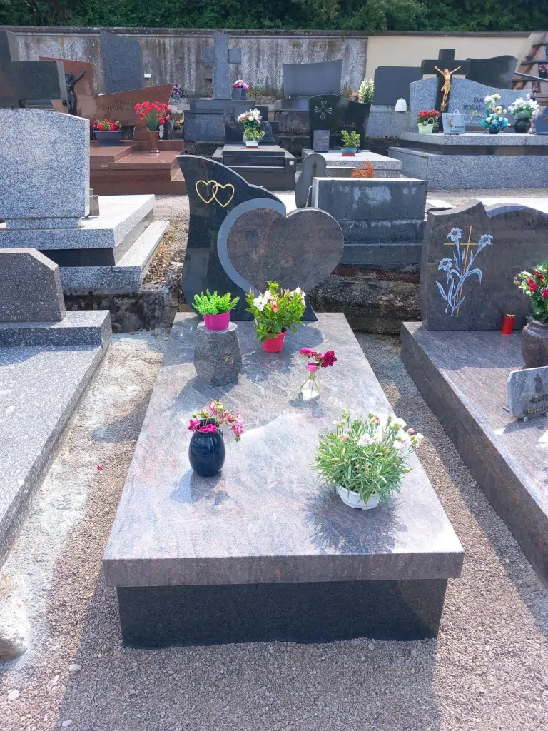 Monument funéraire en granit avec stèle en cœur et pots de fleurs.