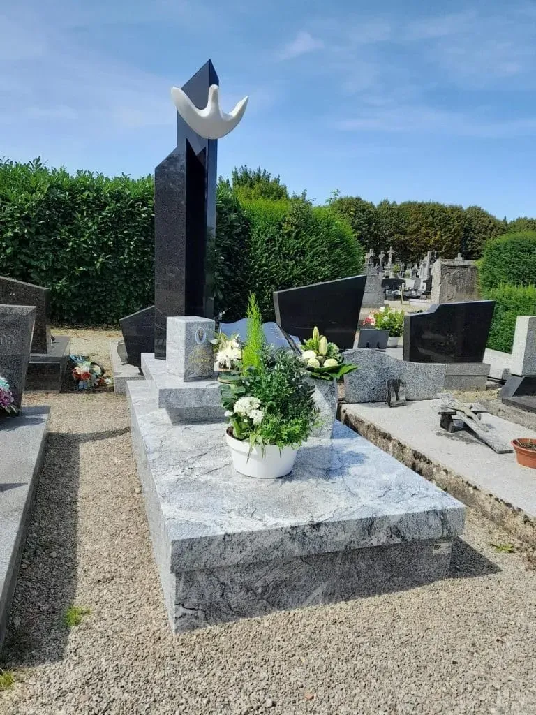 Monument funéraire moderne en granit gris et noir orné de fleurs.