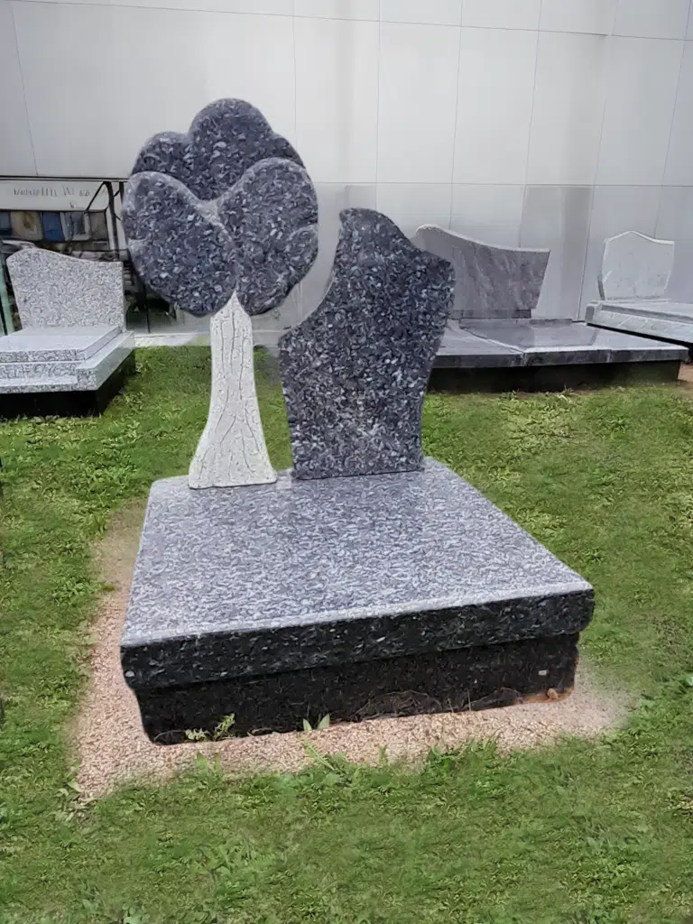 Monument funéraire en granit gris orné d'un arbre sculpté.