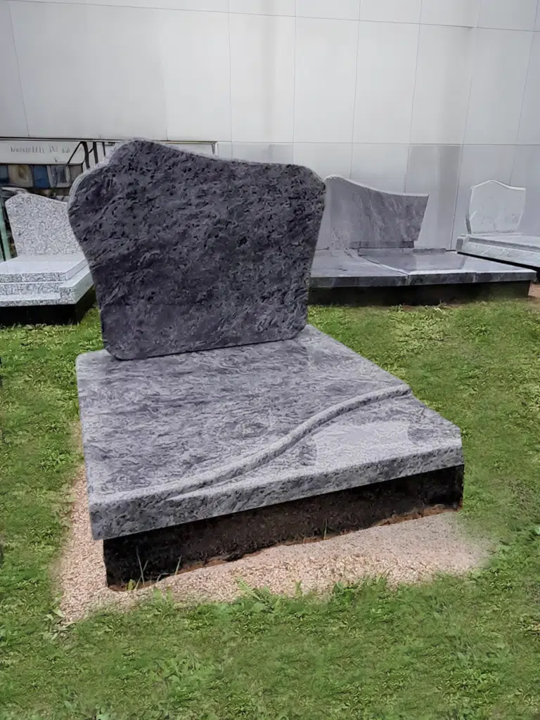 Monument cinéraire en granit gris veiné posé sur un espace vert.